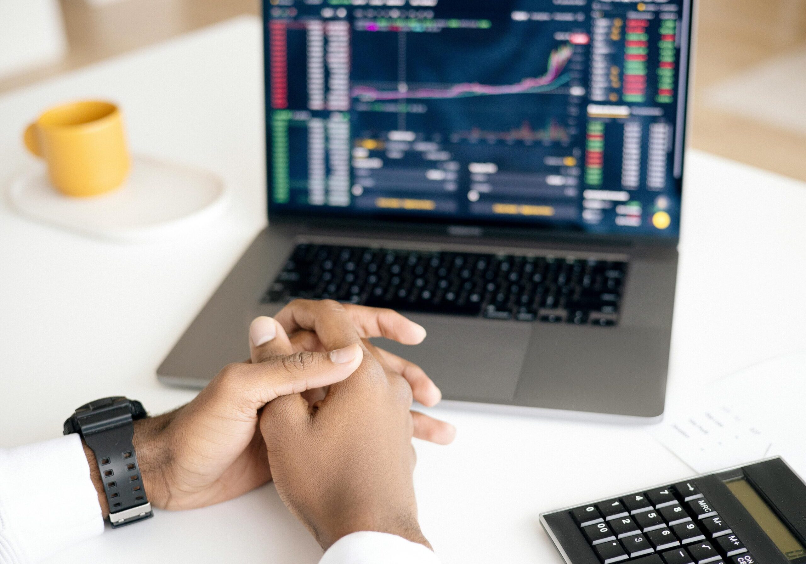 laptop showing stocks, crossed hands